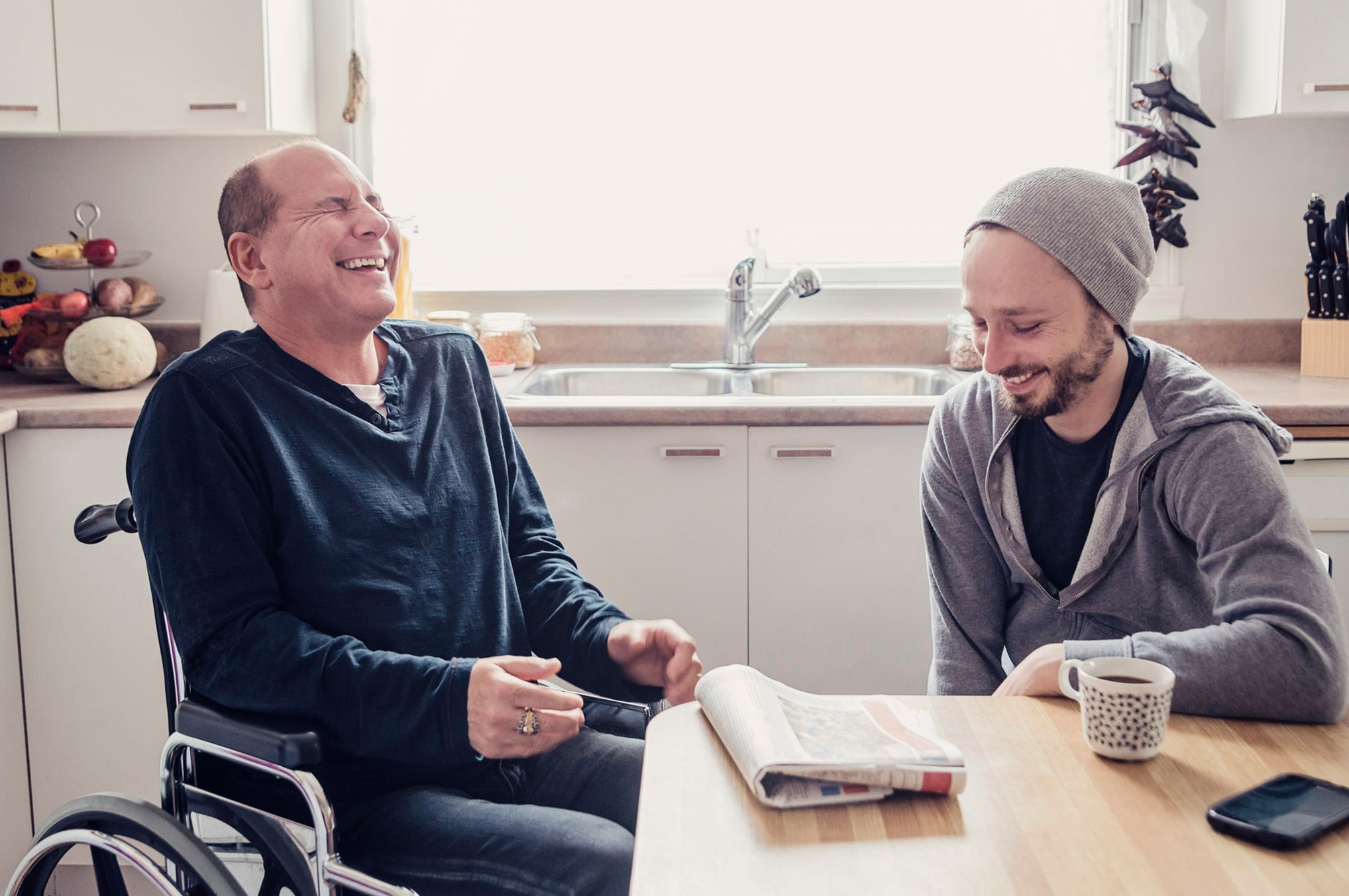 A man in a wheelchair sits beside another man, both engaged in a friendly conversation.