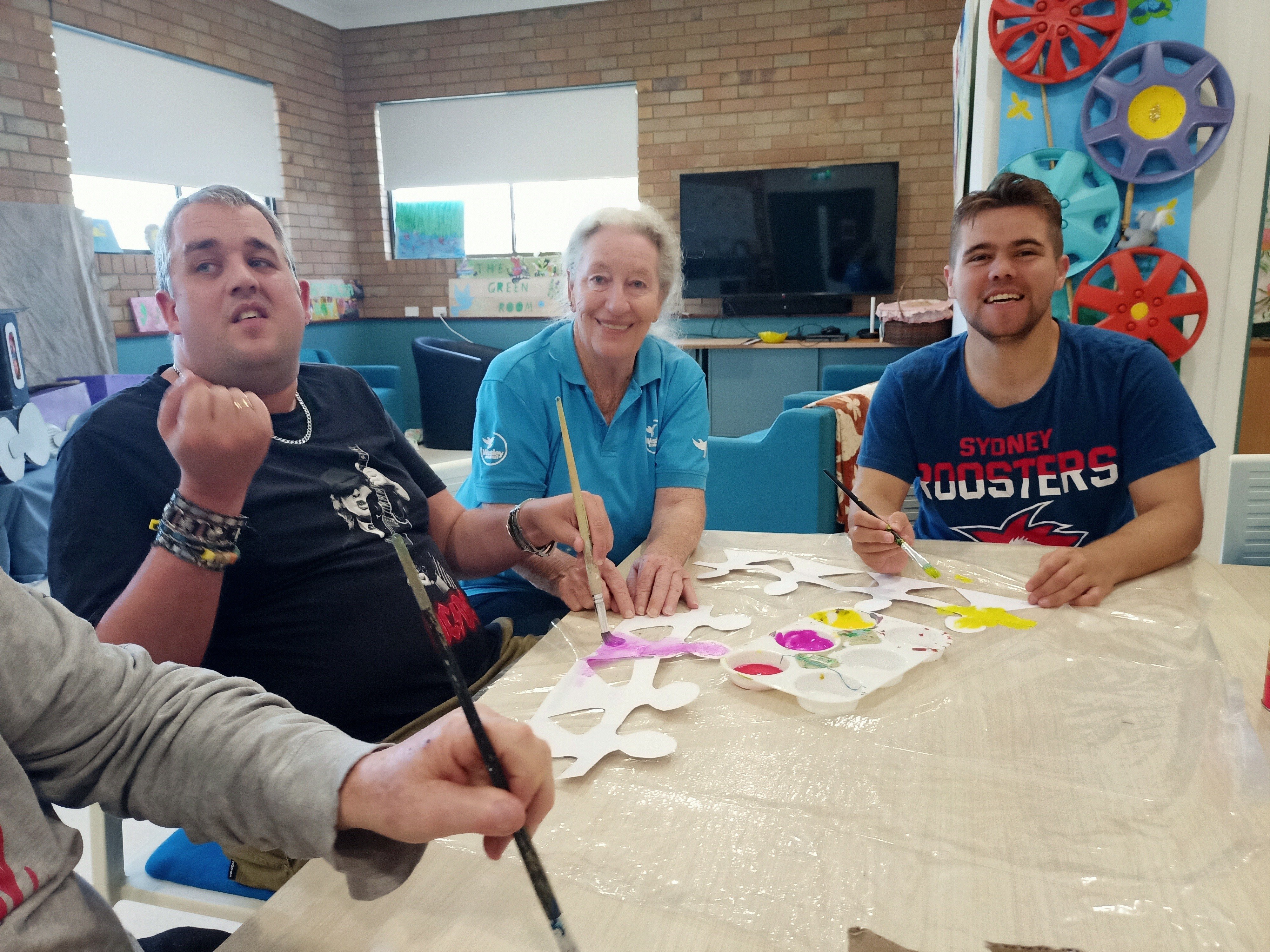 3 people at a table, laughing, painting.