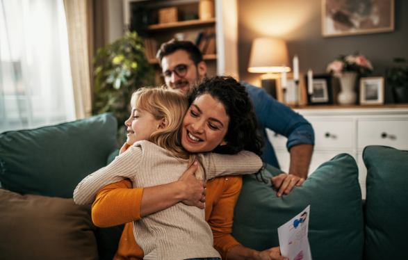 Mother hugging young girl with father in the background - Foster Care